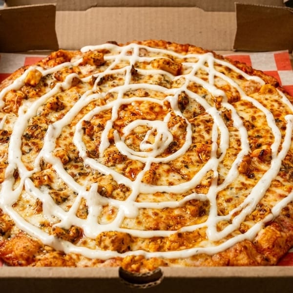 A buffalo chicken pizza with ranch dressing drizzled in a spiral pattern, in a pizza box.
