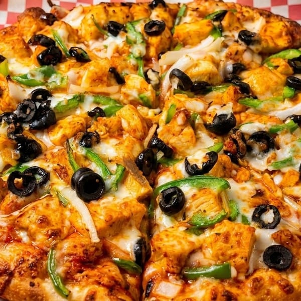 A whole pizza with chicken, black olives, green peppers, and onions in a delivery box.